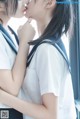 A couple of young women in school uniforms kissing each other.