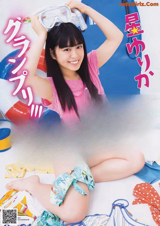 A woman in a pink shirt and blue shorts sitting on a beach.