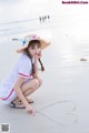 A woman kneeling on the beach with a heart drawn in the sand.