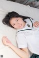 A woman in a school uniform laying on a white blanket.