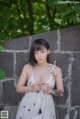 A woman in a white dress standing next to a stone wall.