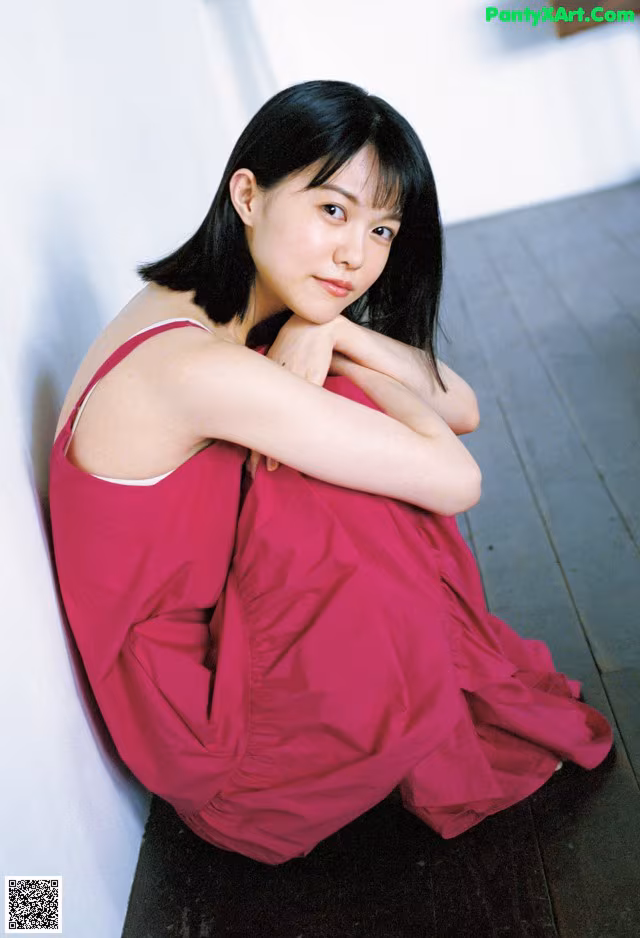 A woman in a pink dress leaning against a wall.