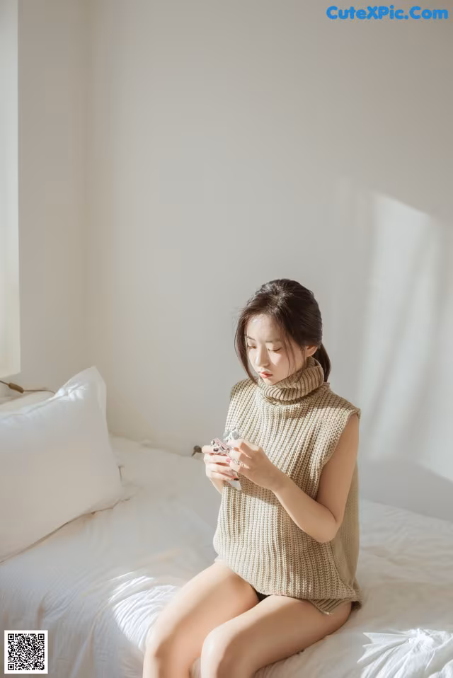 A woman sitting on a bed looking at her cell phone.