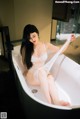 A woman sitting in a bathtub holding a white sheet.