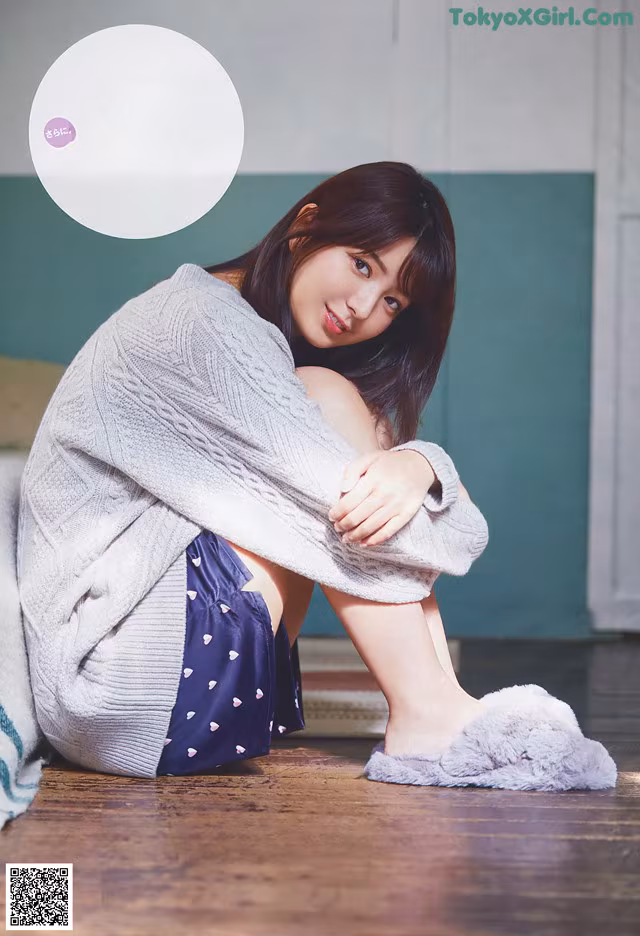 A woman sitting on the floor wearing slippers and a sweater.