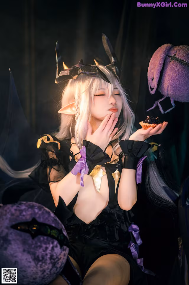 A woman in a black and purple outfit holding a cupcake.