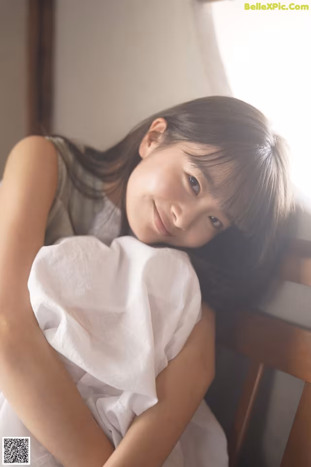 A young girl sitting on a wooden chair with her arms crossed.