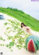 A woman in a bikini laying on a beach next to a watermelon.